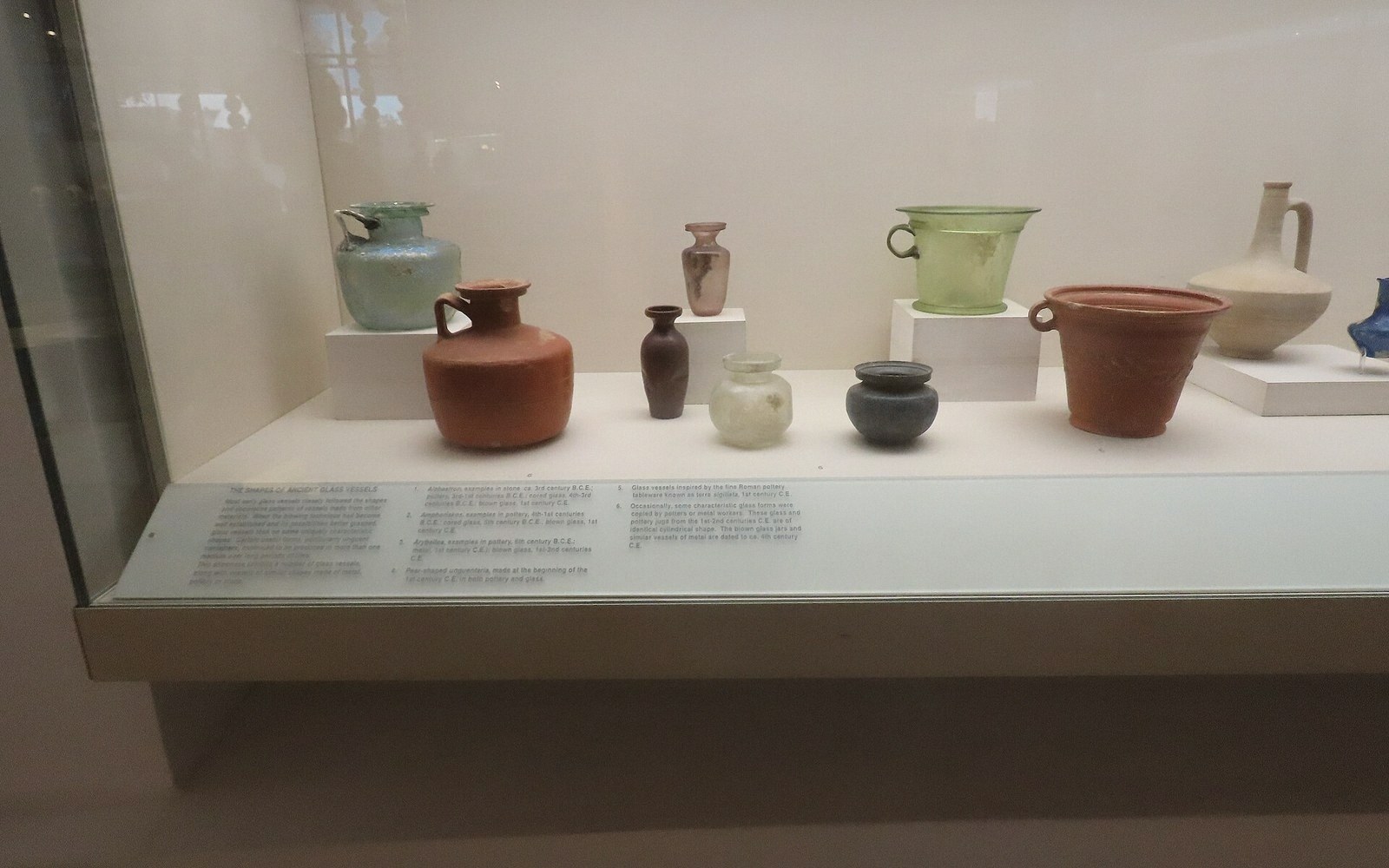 Ancient glass and pottery vessels displayed together in a museum glass case