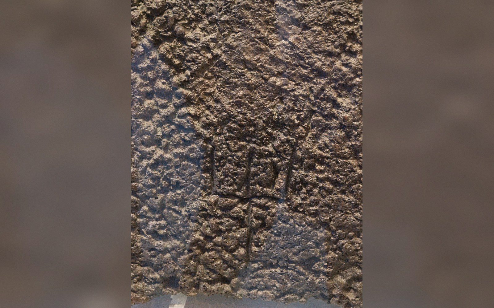 Close-up of a corroded copper ingot with faint incised script markings on its surface