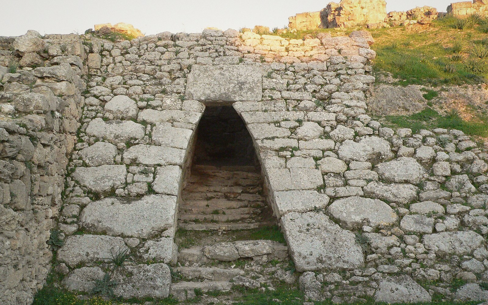 Stone steps lead up through a corbelled tomb entrance in an ancient stone wall
