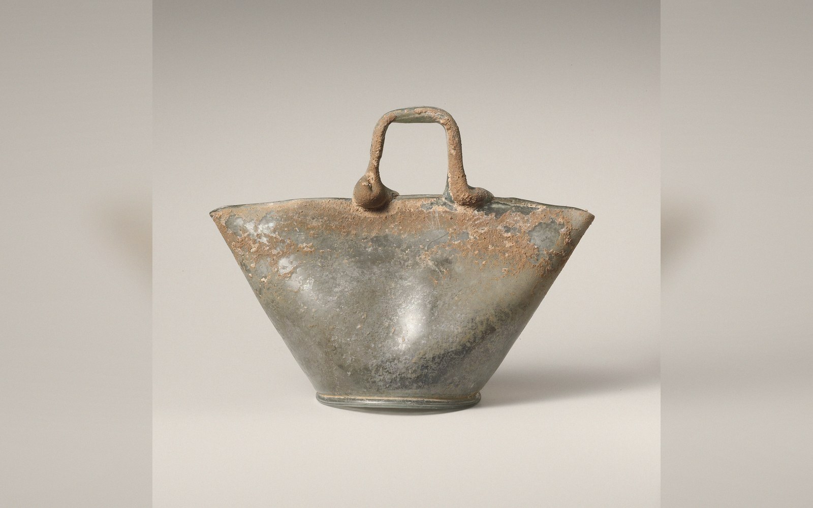 Ancient glass basket-shaped vessel with a flared conical body and looped handle