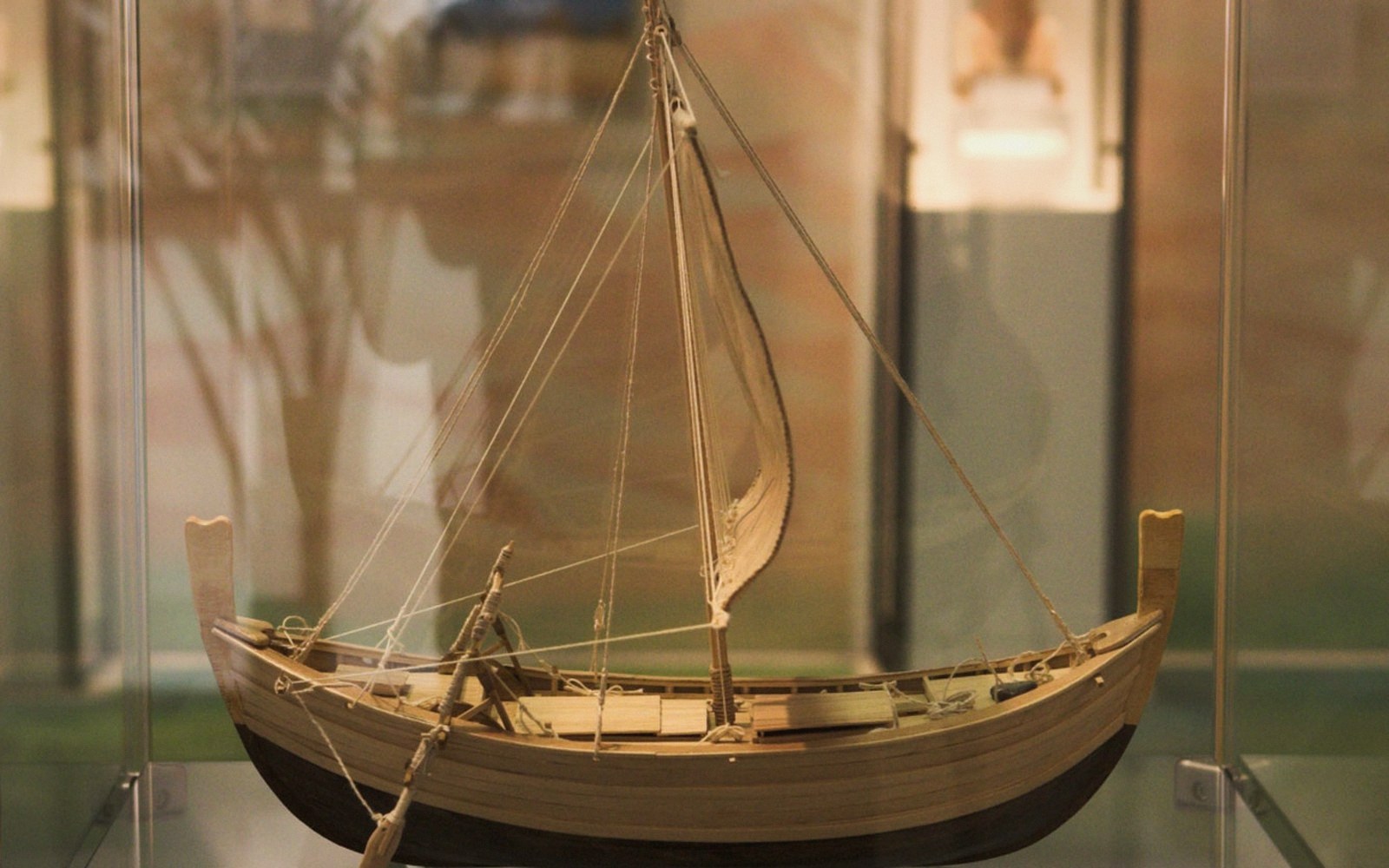 A wooden model ship with a rigged sail displayed in a glass museum case