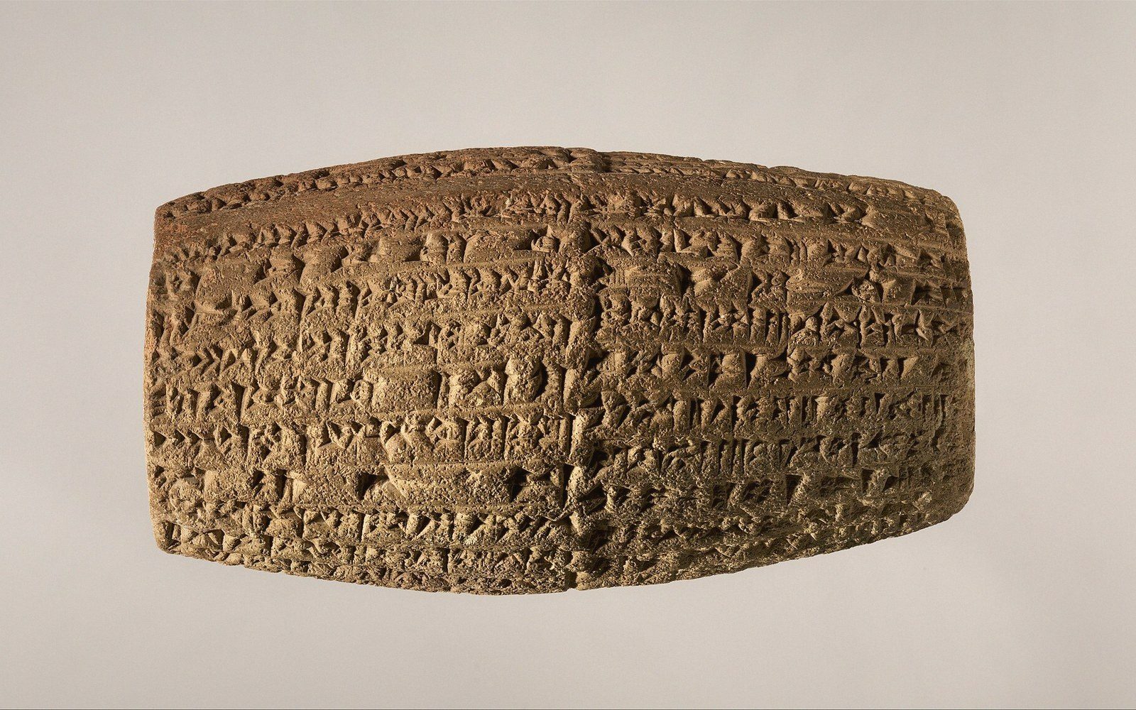 Clay cylinder covered in dense columns of cuneiform inscription
