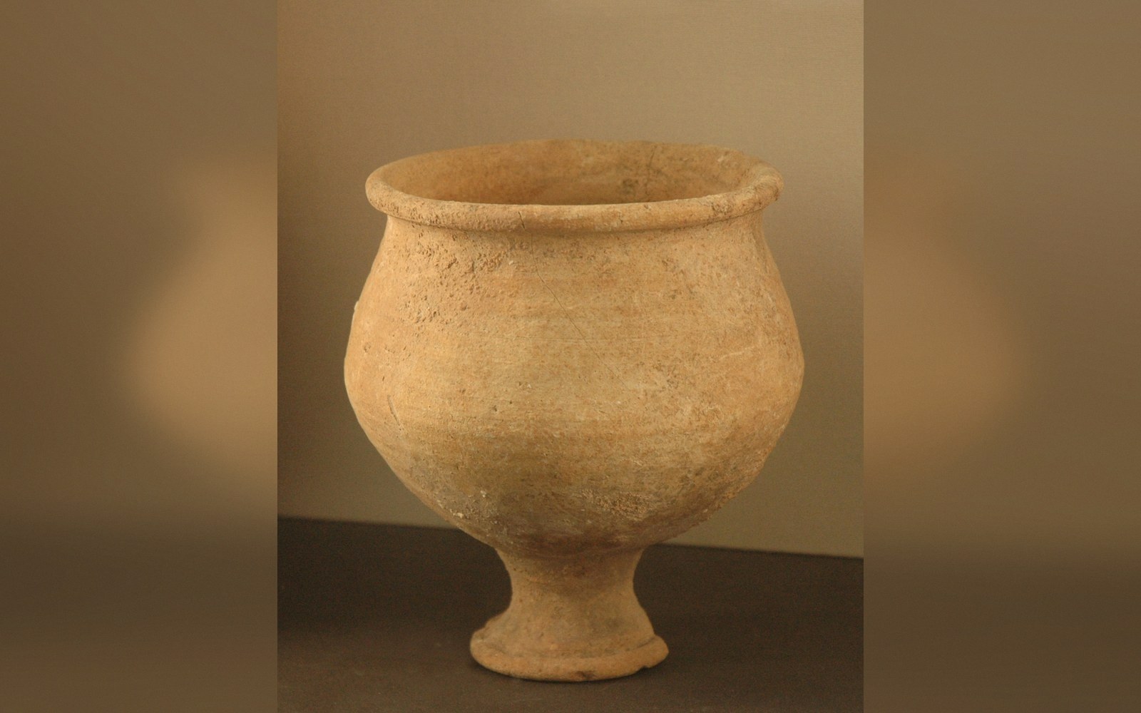Ancient terracotta footed goblet with a wide flared rim, displayed against a plain backdrop