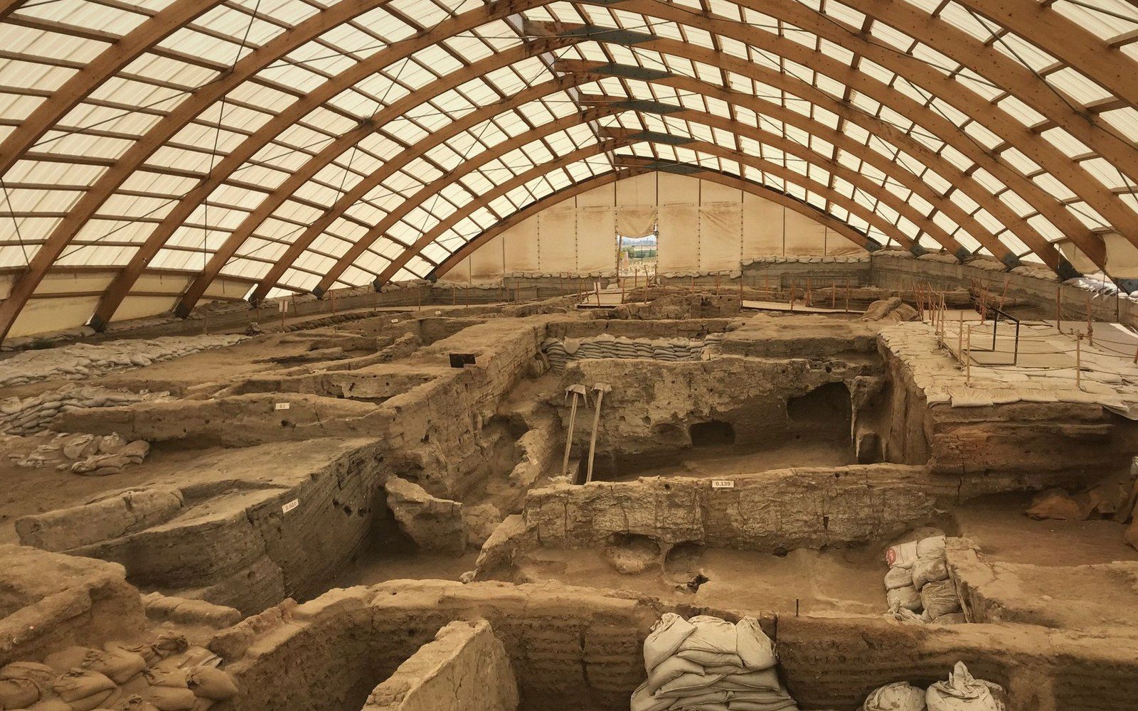 Excavated mudbrick ruins protected under an arched canopy at an archaeological dig site